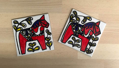 Two square tiles with hand-drawn dala horse decoration.